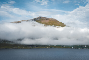 Spectacular views of clouds and fog covering the scenic fjords on the Faroe Islands on the island ov Vagar during a sunny day with blue sky.