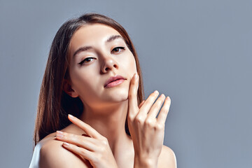 Beautiful young woman with clean perfect skin. Portrait of beauty model with natural nude makeup. Spa, skin care and wellness. Close up, gray background, copyspace.