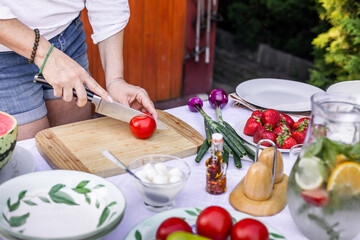 Preparing mediterranean dish for garden party. Woman is chopping red tomato on cutting board for vegetable salad