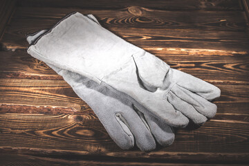 White leather welder gloves on a wooden background. A studio photo with hard lighting.