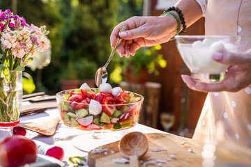 Vegetable salad with mozzarella cheese. Woman preparing mediterranean food on table outdoors