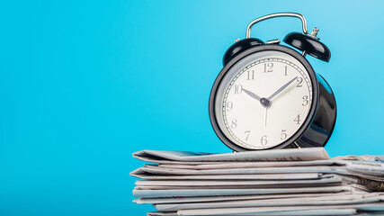 Newspapers and black alarm clock on blue background. Retro alarm clock on newspapers. Media news time concept