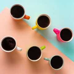 Flat lay some mugs with black coffee on blue and pink paper background.