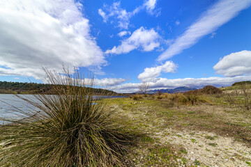Green mountain landscape with blue lake, dirt road and big clouds in the sky, spring atmosphere. Guadalix Madrid.