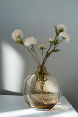 Branch flowers in a glass vase on white table. Decor for interior. 
Jarrón de cristal con flores artificiales