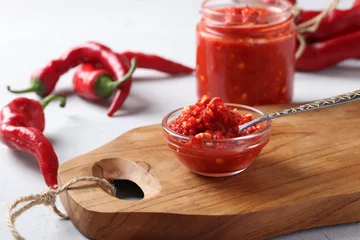 Wall murals Hot chili peppers Traditional sauce adjika with hot chili pepper, paste harissa in bowl on wooden board.