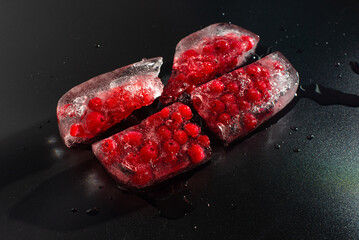 Red currant berries frozen in a piece of broken ice on a black background. Close-up of melting ice briquette