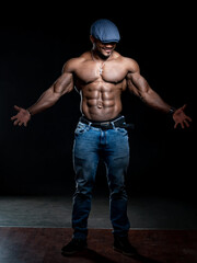 Fototapeta na wymiar Stylish bodybuilder standing like star at studio. Sexy muscular man in blue hat posing for camera.