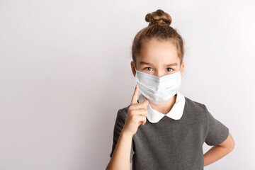 Attractive little girl in a strict school dress, stands on a white background with empty copy space, gestures with her hands, admires a happy expression on her face