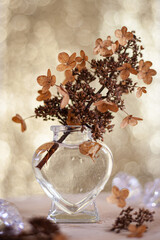 Sprig of dry Hydrangea in a little glass vase and golden bokeh