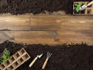 Peat pots and gardening tools are on the ground. Wooden planks in the middle. Copy space. Top view.