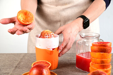 A woman holds a half squeezed orange on her open palm. She holds the juicer with her left hand.