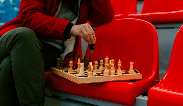 Close up of chess on stadium bleacher. Body part of unrecognizable woman playing in board game in cold weather.