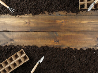 Peat pots and gardening tools are on the ground. Wooden planks in the middle. Copy space. Top view.