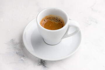 White cup of black espresso coffee on white textured marble background. Close-up shot, top view.