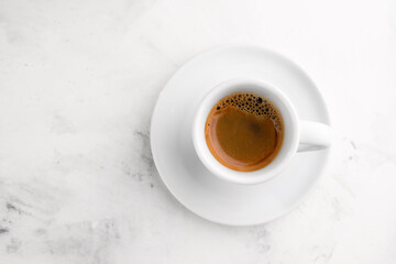 White cup of black espresso coffee on white textured marble background. Close-up shot, top view.