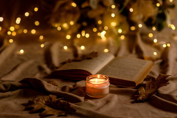 A burning candle on a wooden table in front of a book in a half-mast