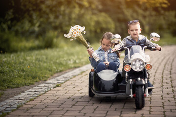 cute preschooler driving little girl in sidecar of motorcycle toy on battery in park