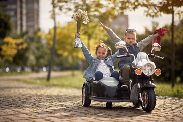 happy kids playing with hands in the air  in autumn park driving motorcycle toy