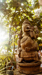 Posąg statua hinduskiego Boga Ganesha, na jasnym roślinnym tle.