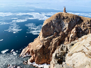 Old lighthouse on rocky coast of the South-east coast of the island of Shkot in winter