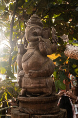 Posąg statua hinduskiego Boga Ganesha, na jasnym roślinnym tle.