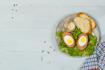 Scotch egg halves on a gray plate with toasted bread, gravy, and lettuce. On a gray wooden background, with space