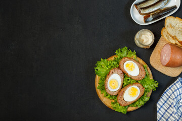 Halves of a Scotch egg on a wooden stand with lettuce leaves.Top view, On a black background, with space