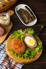 Scotch eggs on lettuce leaves on a dark wooden table with cooking ingredients. Close-up, vertical.