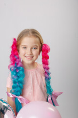 Cute little girl with blond hair and multi-colored bright canecalons with balloons on a light background