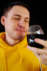 Relaxed young man poses with glass of red wine on black background. Adult happy guy resting with alcohol in his weekend.