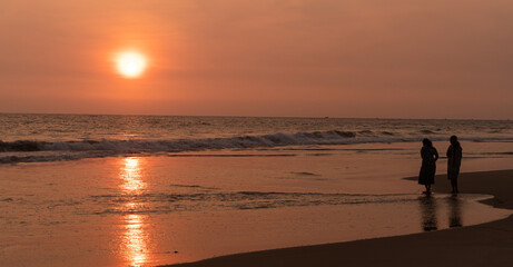 Kobiety spacerujące brzegiem oceanu o zachodzie słońca, ciemno pomarańczowy nastrojowy...