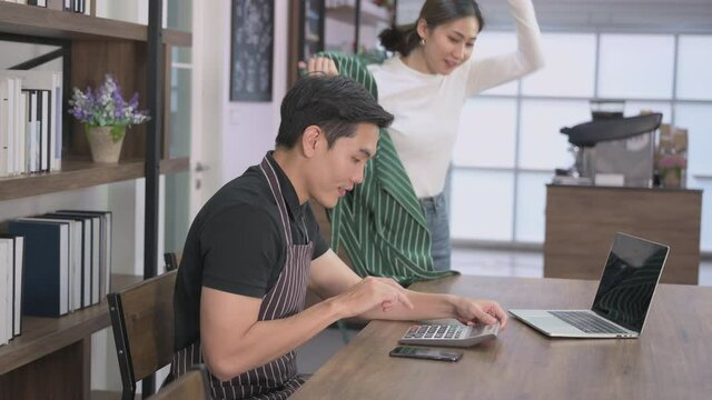 Asian couple owner coffee shop and small business sitting calculating checking balance and costs by using calculator in cafe. Happy young couple barista and fun after profit from coffee shop business.