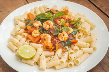 Makaron z krewetkami i sosem warzywnym na białym talerzu, zbliżenie na potrawę, obiad lub lunch. © insomniafoto