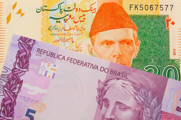 A macro image of a pink and purple five real bank note from Brazil paired up with a orange and green 20 rupee note from Pakistan.  Shot close up in macro.