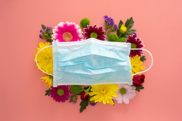 Medical blue face protective mask with colorful flowers on pink background. Creative concept of seasonal allergies. Spring 2021 concept.