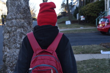 Cool mixed boy in mask and in red hat and with red backpack going to school after pandemic time. Schoolkids in masks.