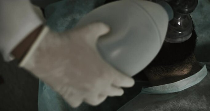 Close up of medics hands putting on ill bearded man oxygen inhalation mask. Top view of unconscious guy in 30s mumbling while lying on medical transportation cart on way to hospital.