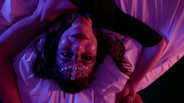 sexy lady with fashion makeup on face is lying on bed at night and looking at camera seductively