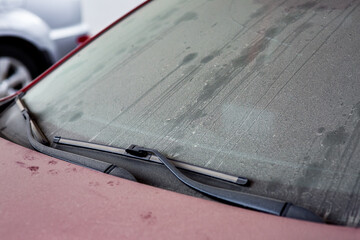 windshield wipers of a dirty red car covered with a layer of dust and dry mud, a closeup of a part of the vehicle, nobody.
