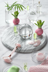 Gua Sha massager and rose quarz face roller on marble stone background. Face care products, glass crystal ball, palm leaves, hyacinth flowers. Skincare tonic, fragrance, soap, essential oil and serum.