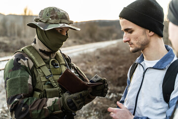 Armed soldier in uniform checking documents of suspect migrant or terrorist arrest during patrol in...