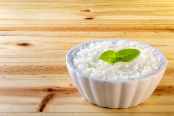 UMA BACIA COM ARROZ BRANCO E FOLHAS DE MANJERICÃO, SOBRE A SUPERFÍCIE DE MADEIRA.
