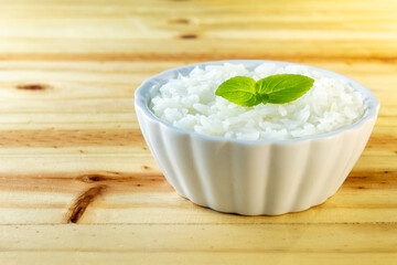 UMA BACIA COM ARROZ BRANCO E FOLHAS DE MANJERICÃO, SOBRE A SUPERFÍCIE DE MADEIRA.
