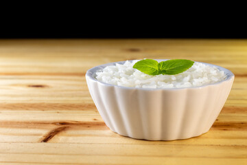 UMA BACIA COM ARROZ BRANCO E FOLHAS DE MANJERICÃO, SOBRE A SUPERFÍCIE DE MADEIRA.
