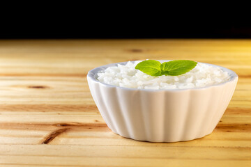 UMA BACIA COM ARROZ BRANCO E FOLHAS DE MANJERICÃO, SOBRE A SUPERFÍCIE DE MADEIRA.
