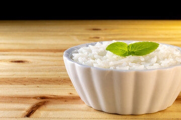 UMA BACIA COM ARROZ BRANCO E FOLHAS DE MANJERICÃO, SOBRE A SUPERFÍCIE DE MADEIRA.
