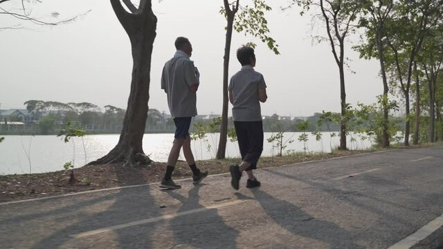 happy senior couple holding hand and walking exercise at park in evening sunset. smiley active asian elderly lover outdoor activity sharing good moment together. fitness duo mature workout at park.