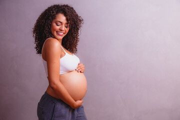 Beautiful pregnant Afro woman, posing for photo showing her pregnancy belly, smiling for the photo...