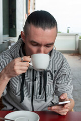 young man drinking a cup of coffee in a cafe and looking at the phone